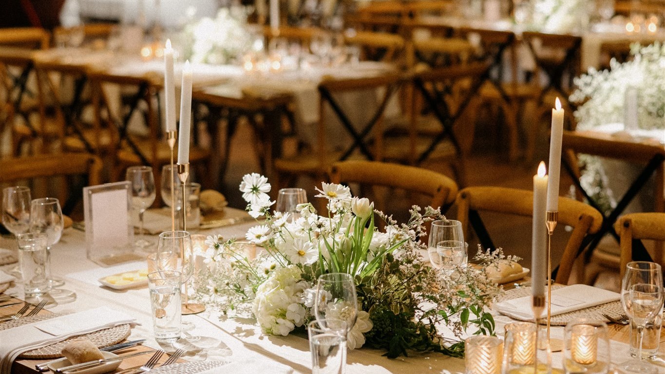 Long reception table with a low white floral centrepiece and taper candles